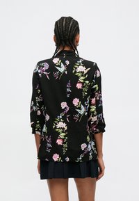 Fekete virágos ing, színes virág- és levélmintákkal, galléros nyakkivágással és háromnegyedes ujjakkal.