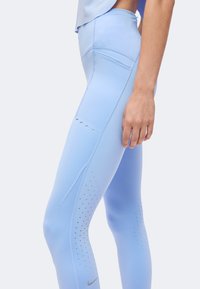 Gros plan d'une personne portant des leggings taille haute bleu clair avec une poche latérale et de petits trous de ventilation sur les jambes.
