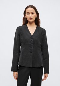 Čierne, na mieru ušité sako s výstrihom do V, dlhými rukávmi a piatimi kruhovými gombíkmi. Má štruktúrovaný živôtik a hladkú textúru.