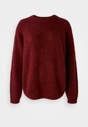 Punainen neulepaita, jossa on pyöreä pääntie, pitkät hihat ja pehmeä rakenne. Mallissa on rento istuvuus ja se laskeutuu hieman helmasta.