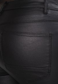Pantalons en simili cuir noir avec une texture lisse, dotés d'une poche arrière, de coutures décoratives et d'un design slim et ajusté.