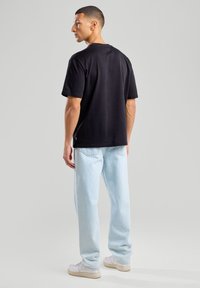 La t-shirt nera in cotone presenta maniche corte e una vestibilità rilassata. Abbinata a jeans in denim blu chiaro, completata da sneakers bianche.