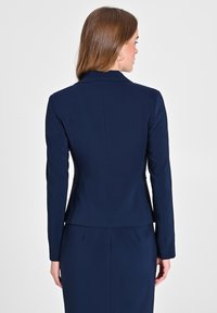 Navyblauer, taillierter Blazer mit langen Ärmeln, Reverskragen und einer figurnahen Form, der eine glatte Textur und eine Rückennaht-Detailierung aufweist.