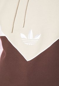 Hoodie s dizajnom u boji tamno smeđa i svijetlo smeđa, od mekog materijala, s podesivim vezicama i bijelim izvezenim logom sprijeda.