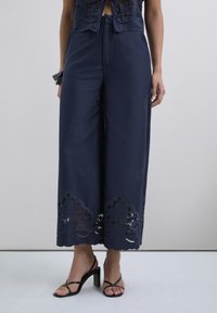 Pantalones de pierna ancha en color navy con bordado floral y detalles de encaje en el dobladillo, con una textura suave y un ajuste relajado.