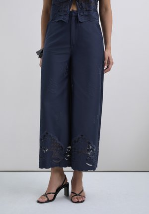 Pantalones de pierna ancha en color navy con bordado floral y detalles de encaje en el dobladillo, con una textura suave y un ajuste relajado.