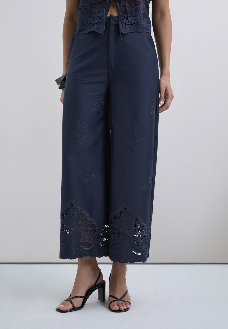 Pantalones de pierna ancha en color navy con bordado floral y detalles de encaje en el dobladillo, con una textura suave y un ajuste relajado.