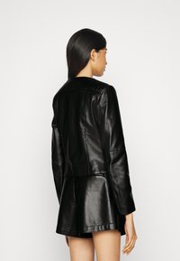 Giubbotto di pelle nera con colletto a coste e silhouette aderente, caratterizzato da una superficie liscia e un design su misura, con dettagli di cucitura visibili.