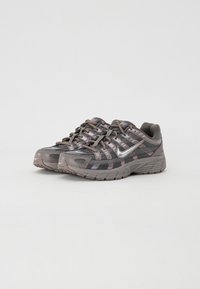 Chaussures de sport grises avec un tissu en maille, des accents réfléchissants et une semelle en caoutchouc texturée. Présente un laçage avec des motifs multicolores sur les côtés.