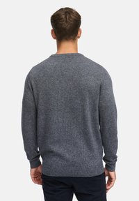 Grå strikkegenser med lange ermer og rund hals. Har ribbede mansjetter og nederkant. Myk tekstur, ensfarget design uten mønstre.