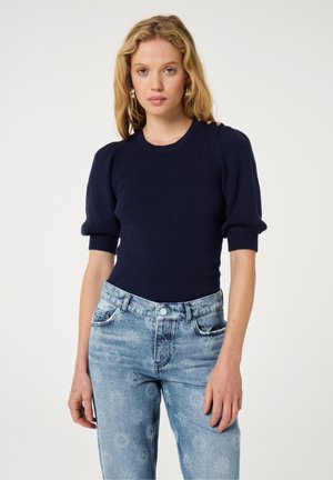 Marineblaues, geripptes Strickoberteil mit Ballonärmeln, kombiniert mit hellblauen Jeans mit floralem Muster. Insgesamt glatte Textur.