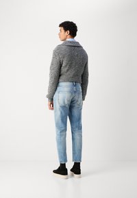 Pull en maille grise coupé avec un col large, associé à un jean en denim bleu clair et des baskets en suède noir avec une épaisse semelle blanche.