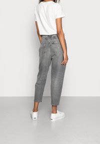 Szare jeansy z wysokim stanem, zwężającą się nogawką, pięcioma kieszeniami i postarzanym wykończeniem, zestawione z białym t-shirtem i białymi sneakersami.