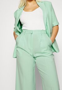 Blazer vert menthe et pantalon large assorti, présentant une texture lisse et une coupe ajustée, associés à un débardeur blanc.