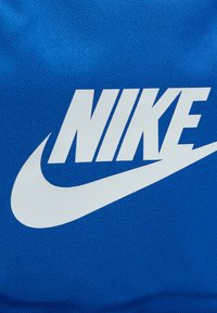 Μπλε υφασμάτινη τσάντα με έντονο λευκό λογότυπο Nike και σχεδιασμό με swoosh. Το υλικό φαίνεται ανθεκτικό με υφή.