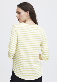 Triibuline särk valge ja heledate kollaste triipudega, 3/4-sleeve'd, ümar kaelus, pehme materjal, külgmised lõhikud ja kumer hem taga.