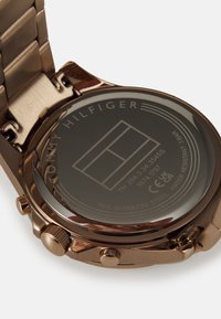 Montre en acier inoxydable rose gold avec un cadran rond, des boutons-poussoirs et des détails gravés à l'arrière, incluant le logo de la marque et l'indice de résistance à l'eau.