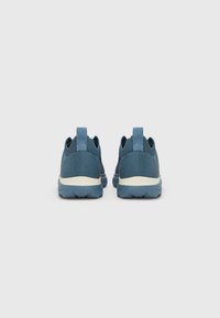 Ζευγάρι μπλε παπουτσιών τύπου slip-on με λευκές μεσαίες σόλες, εμφανιζόμενα από πίσω σε ένα απλό ανοιχτό γκρι φόντο.