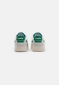 Hvite og grønne sneakers med overdel av semsket skinn og lær. Funksjoner inkluderer en teksturert såle, grønne detaljer og en logo på hælen.