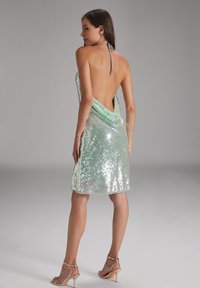 Paillettenjurk in pastelgroen met een halterhals. Ontwerp met een open rug, gedrapeerde stof valt tot halverwege de dij. Zilveren hakken maken de look compleet.