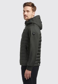 Dunkelgrüne Pufferjacke mit Kapuze, horizontal gestepptem Design, mit Reißverschlusstaschen, verstellbaren Kordelzügen und einem runden Logo am Ärmel.
