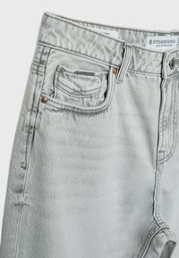 Jean en denim gris clair avec poche avant, petite poche, passants de ceinture, fermeture par bouton et détails de couture apparents.