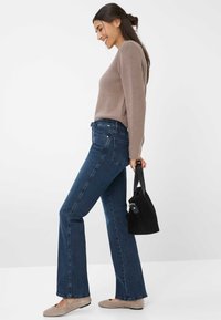 Lichtbruine trui, donkerblauwe flared jeans, beige ballerina's en een kleine zwarte handtas. Gladde textuur en eenvoudig ontwerp. Duidelijke achtergrond.