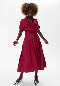 Fuchsia wikkeljurk met korte mouwen en een ceintuur rond de taille. Vloeiende rok, zachte stof en schoenen met dierenprint maken de look compleet.