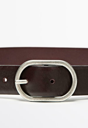 Burgundský kožený opasek s velkou oválnou stříbrnou kovovou přezkou s texturovaným povrchem a několika nastavovacími otvory podél pásku.
