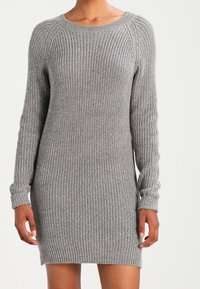 Grå stickad klänning med långa ärmar, ribbad textur och rund halsringning. Kort längd och tajt passform vid ärmsluten och nederkant.