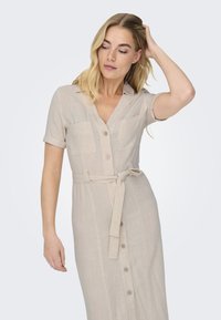 Beige linnen skjortekjole med korte oppbrettede ermer, to fremre lommer og knyttet belte, med knapper foran.