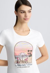 T-shirt en coton blanc avec une illustration colorée de scène de plage représentant deux chaises, un parasol, et le texte "Summer Vibes LIU-JO SE DISTINGUE."