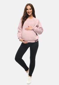 Felpa rosa chiaro in morbido tessuto, caratterizzata da una vestibilità comoda e polsini a costine, abbinata a leggings neri e sneakers bianche.