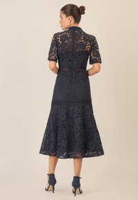 Abito in pizzo blu navy con motivi floreali, maniche corte, corpetto aderente e gonna a ruota. Abbinato a tacchi blu navy.