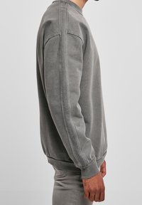 Sudadera gris de mezcla de algodón, con mangas largas, puños acanalados y cuello redondo. Textura suave con detalles de diseño mínimos.