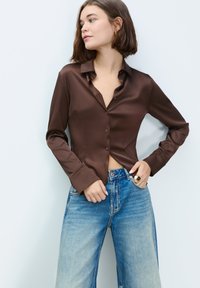 Brown satin shirt with a collar, button-down front, and long sleeves, paired with light blue wide-leg denim jeans.
