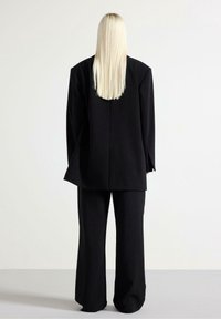 Blazer nero sartoriale con vestibilità morbida, spalle marcate e pantaloni abbinati a gamba dritta. Tessuto liscio e dettagli di design minimali.