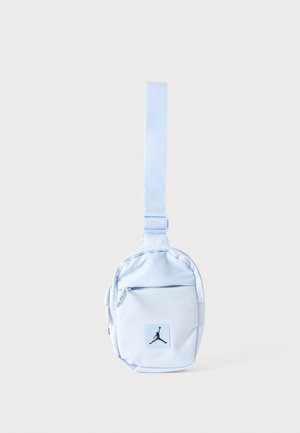 Világoskék kompakt oldaltáska állítható pánttal, elülső cipzáras zsebbel és fekete Jumpman logóval az elülső zsebén.