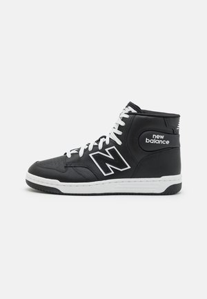 Mustavalkoinen korkea New Balance tennari, jossa valkoiset nauhat ja logo sivussa, esitetty ulkopuolelta tummalla taustalla.