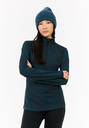 Langsleeve zip-up top, zwart en teal zebra patroon, zachte stof, hoge kraag. Gecombineerd met een blauwe gebreide muts.