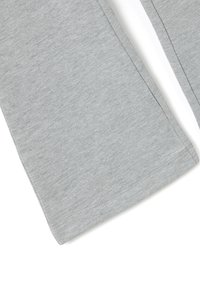Primer plano de unos pantalones de tela gris que muestran una costura detallada a lo largo del dobladillo y la costura lateral sobre un fondo blanco.