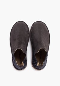 Pareja de zapatos slip-on de ante marrón oscuro con puntas redondeadas y paneles de talón negros brillantes, vistos desde arriba sobre un fondo blanco.