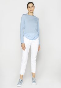 Jasnoniebieska bluzka z długim rękawem i okrągłym dołem, zestawiona z białymi, krótkimi spodniami oraz jasnoniebieskimi adidasami z dekoracyjnymi akcentami.