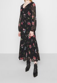 Robe longue noire à fleurs avec de longues manches transparentes, présentant des fleurs multicolores, un décolleté en V, une taille cintrée et un ourlet fluide en étages.