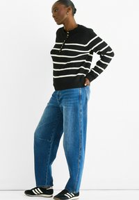 Black and white striped knitted sweater with a crew neckline and button placket, paired with high-waisted, loose blue denim jeans and black sneakers.