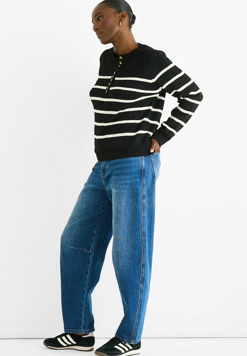 Black and white striped knitted sweater with a crew neckline and button placket, paired with high-waisted, loose blue denim jeans and black sneakers.