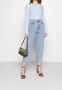 Světle modrý top s dlouhým rukávem v kombinaci s džínami s vysokým pasem a rovnými nohavicemi. Doplněno malou olivově zelenou kabelkou a černými sandály na podpatku.