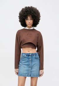 Rjava kratka majica z rebrastim izrezom in reliefnim vzorcem, kombinirana z modro jeans minikilitico s sprednjim zapiranjem na gumbe.