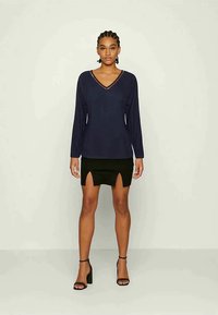 Top de manga longa azul-marinho com decote em V e renda, combinado com uma saia mini preta com fendas frontais, complementado por sandálias de salto alto pretas.