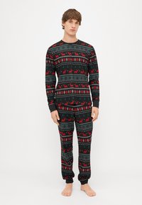 Black pajama set featuring a geometric pattern with red reindeer, green trees, and white snowflakes; soft fabric with long sleeves and cuffs.